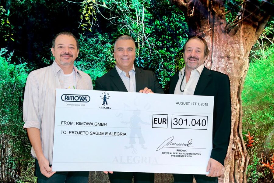 Sérgio Barreto, diretor executivo da RIMOWA BRASIL (centro) entrega o cheque para Caetano (esquerda) e Dr. Eugênio Scannavino Netto, do Projeto Saúde e Alegria (direita)
