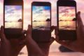 Três mãos segurando celulares enquanto fotografam o mar e céu