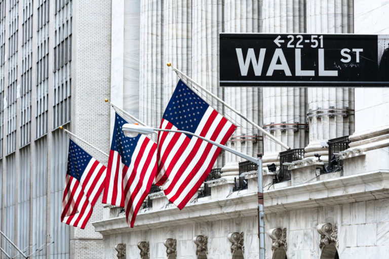 Bandeiras dos estados Unidos atrás de uma placa de rua que indica Wall Street