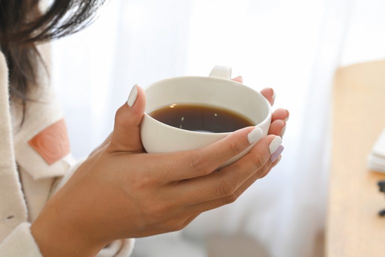 Mão de uma mulher segura uma xícara branca com café