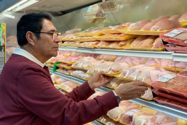 Consumidor no supermercado escolhendo cortes de frango em uma gôndola de produtos