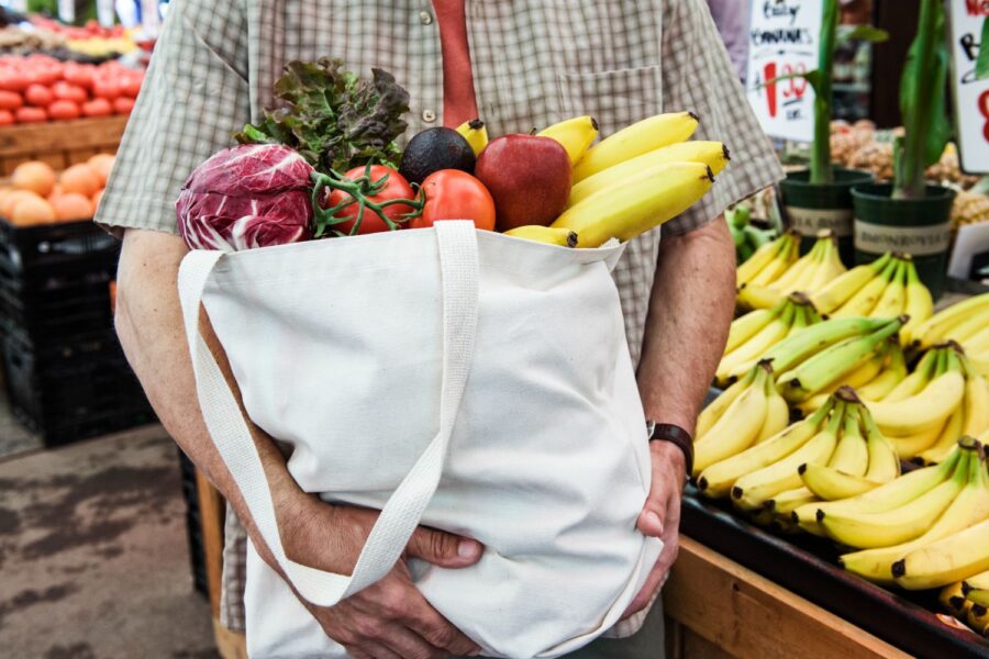 homem em uma feira livre segurando um sacola de frutas e legumes