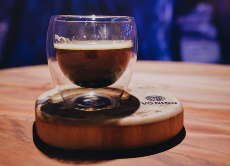 Xícara de café em vidro transparente, apoiada em base de madeira como pires