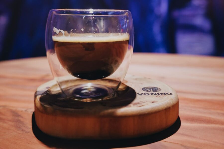 Xícara de café em vidro transparente, apoiada em base de madeira como pires