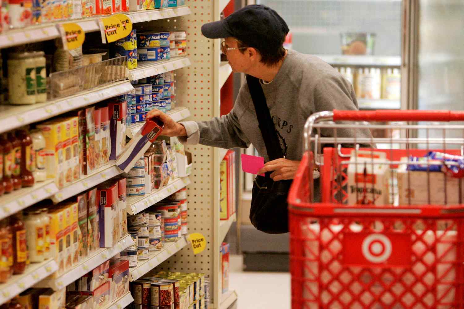 Imagem mostra uma pessoa fazendo compras em um mercado, com um produto na mão