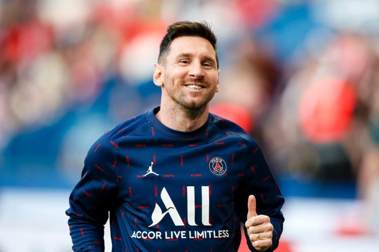 Jogador de futebol Lionel Messi sorrindo em campo com camiseta do PSG