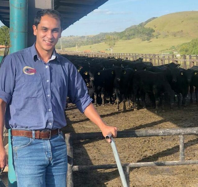 Carletto vez jeans e camisa azul. Está em um confinamento de animais angus 