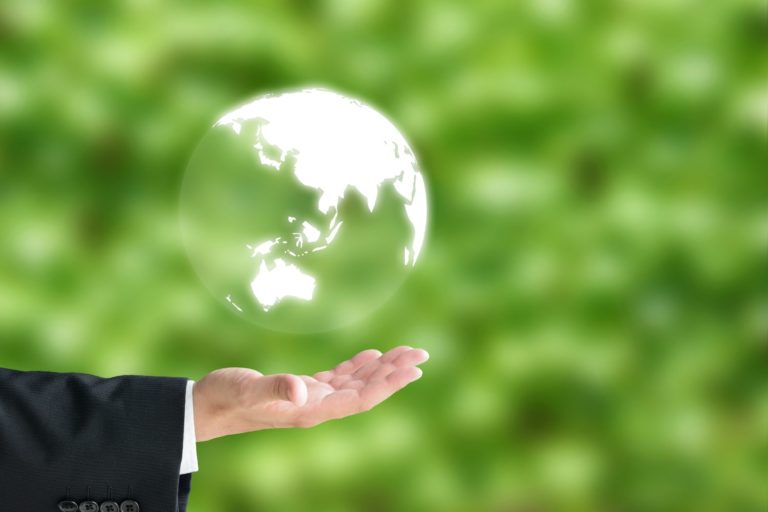Mão com uma pessoa de terno segurando um globo terrestre sobre um fundo verde desfocado