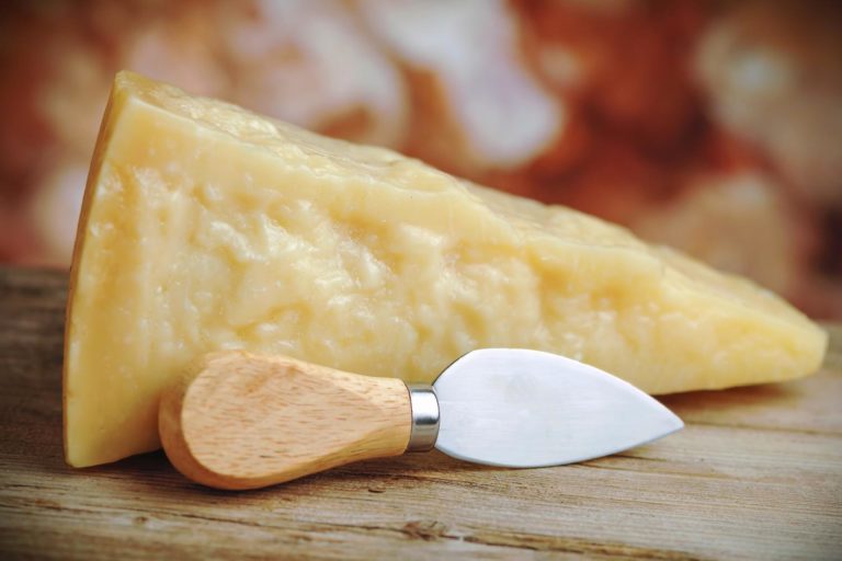 pedaço de queijo parmesão sobre uma tábua de queijos, com um cortador ao lado