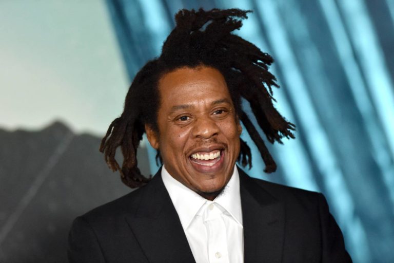 Retatro de Jay Z sorrindo usando terno preto sobre camisa branca