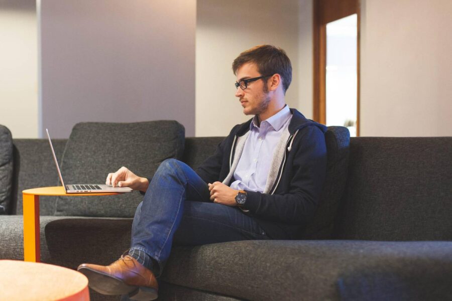 Imagem mostra um homem trabalhando no sofá, apoiando o notebook em uma mesa