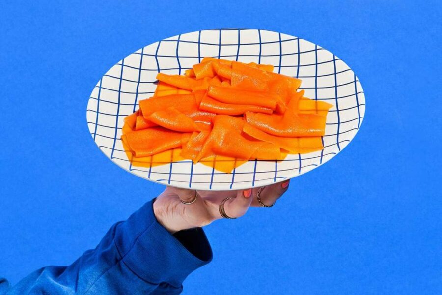 Cena aparece uma mão segurando um prato onde há lascas de peixe plant based