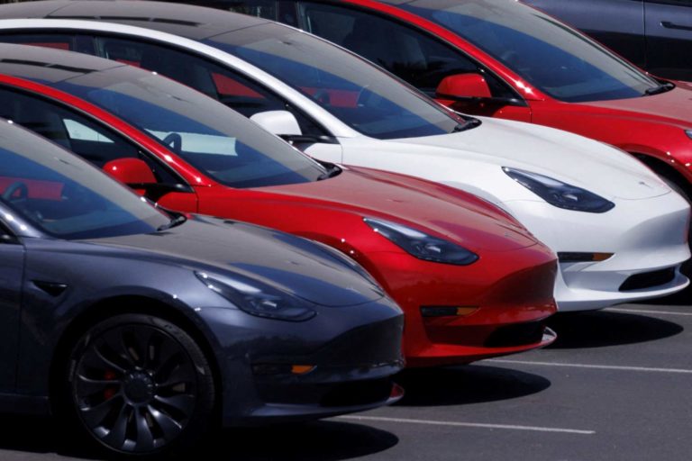 Foto mostra quatro veículos da Tesla, sendo um cinza, dois vermelhos e um branco