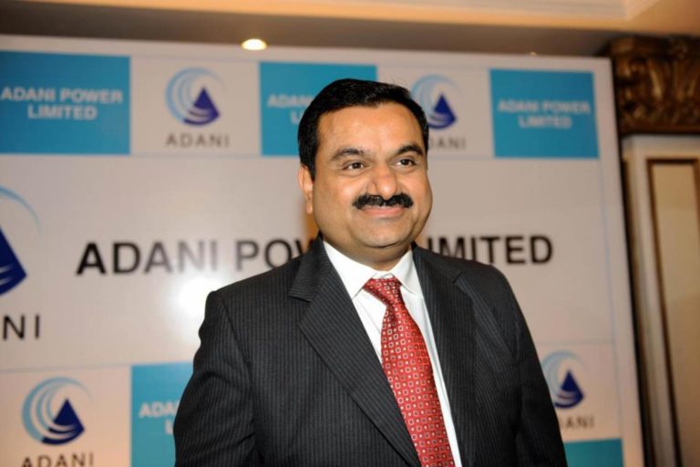 Gautam Adani tem bigode e cabelos pretos. Ele usa terno e gravata e sorri para a foto.