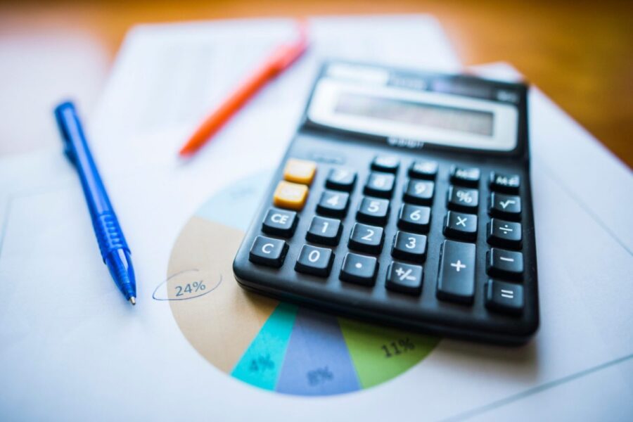 Calculadora, caneta e papel, com um desenho de gráfico, em cima de uma mesa 