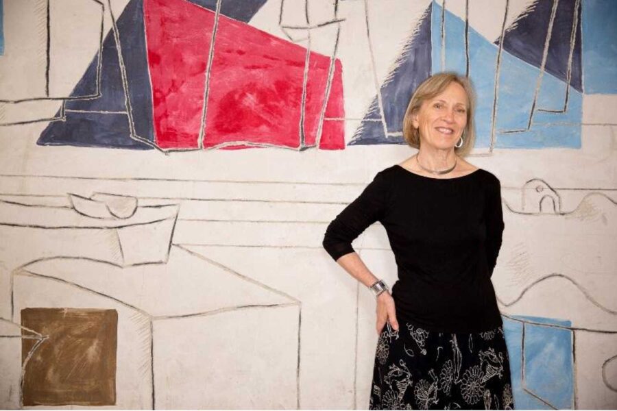 Claudia Goldin, senhora vestida de preto em frente a um quadro, é autora de um livro sobre carreiras femininas