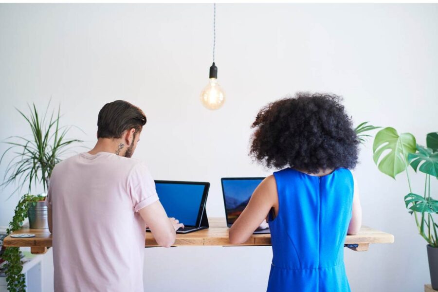 Homem e mulher trabalham lado a lado em computadores.