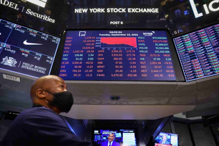 Homem em frente a tela com índices de Wall Street