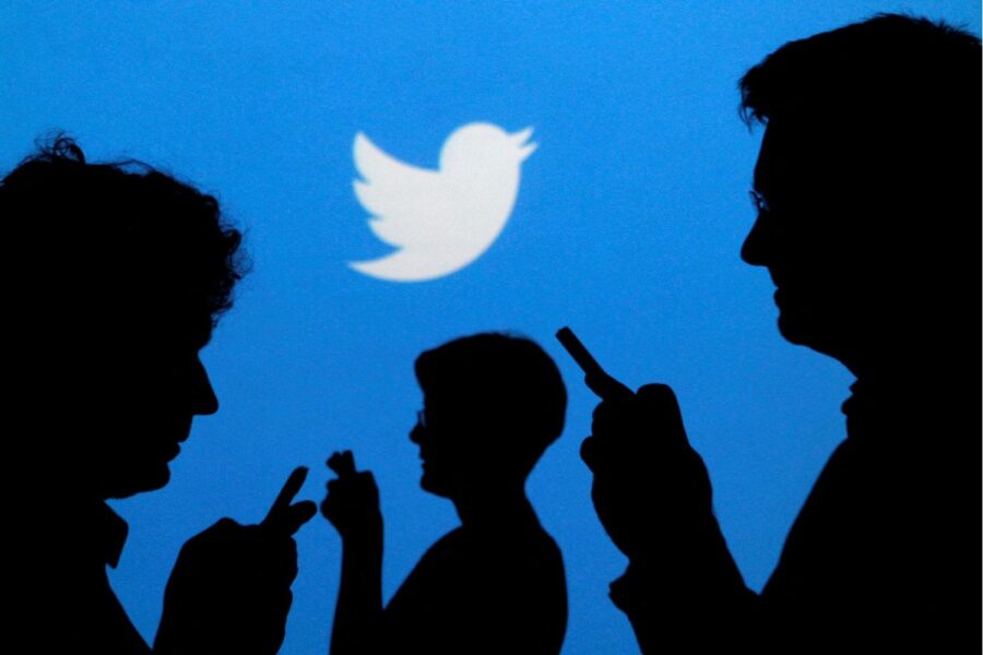 Sombras de pessoas segurando celulares em fundo com a logo do Twitter