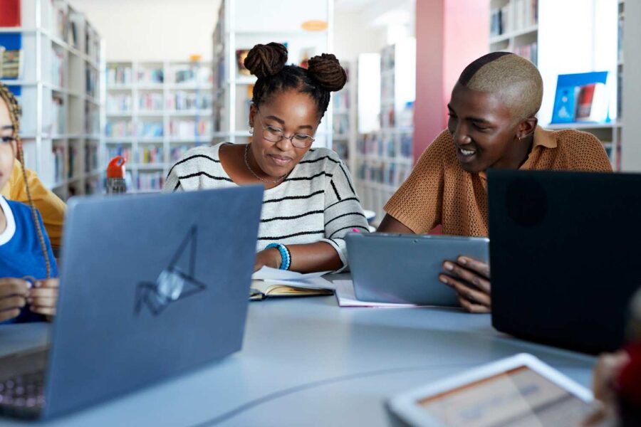 Dois estudantes sentados mexendo no computador em uma biblioteca