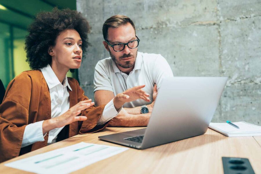 Mulher aponta para uma tela de computador e conversa com um homem ao seu lado
