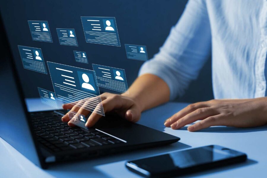 Pessoa mexendo em um computador com perfis de pessoas na tela e um celular ao lado