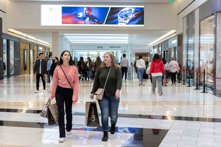 Mulheres com sacolas nas mãos andam por centro comercial