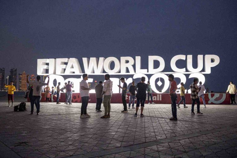 Pessoas estão em pé na frente do letreiro luminoso da Copa do Mundo no Catar 