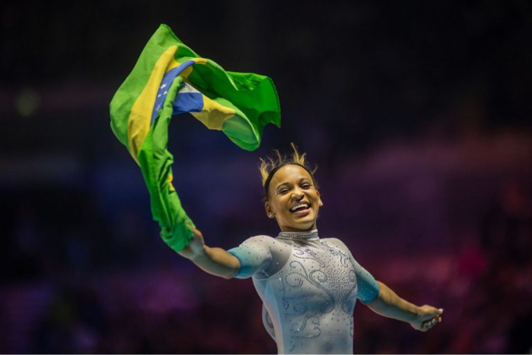 a ginasta rebeca andrade no mundial de ginástica erguendo uma bandeira do brasil