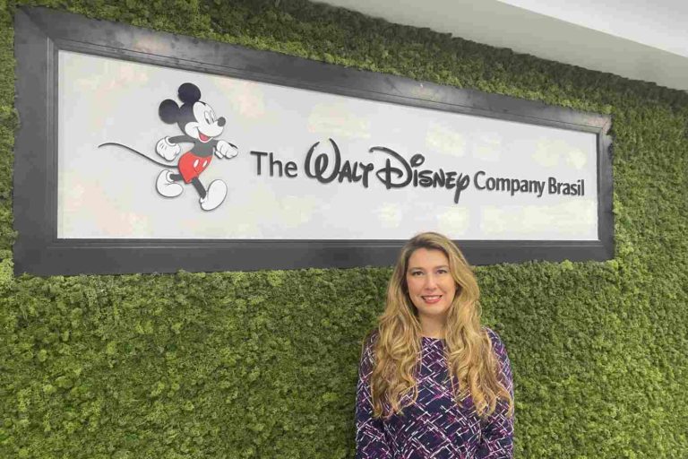 Mulher sorri e olha para a câmera em frente a letreiro da The Walt Disney Company Brasil