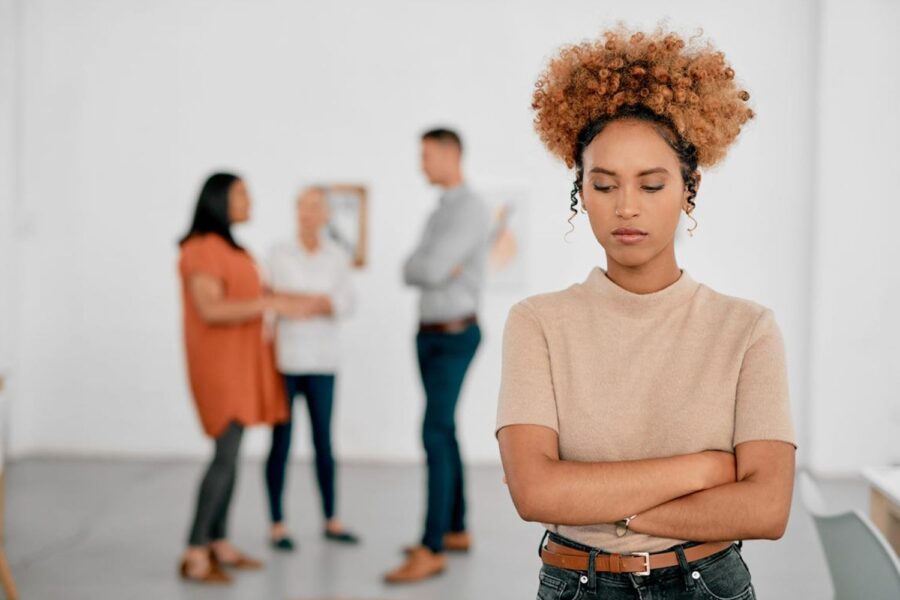 mulher negra triste com colegas de trabalho ao fundo