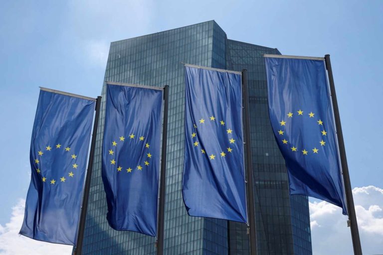 Bandeiras da União Europeia em frente a prédio espelhado