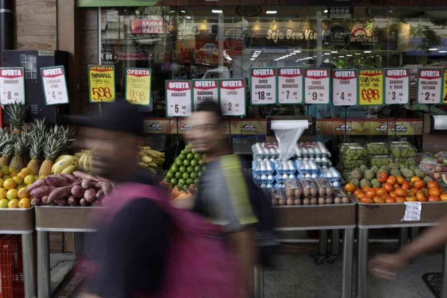 Pessoas andando na frente de barracas de frutas na feira