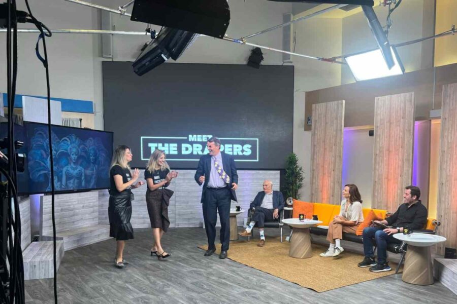 Tim Draper de pé e conversando com pessoas em programa de televisão
