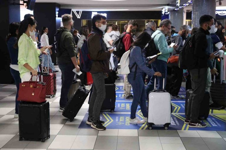 Pessoas de máscara em fila de aeroporto