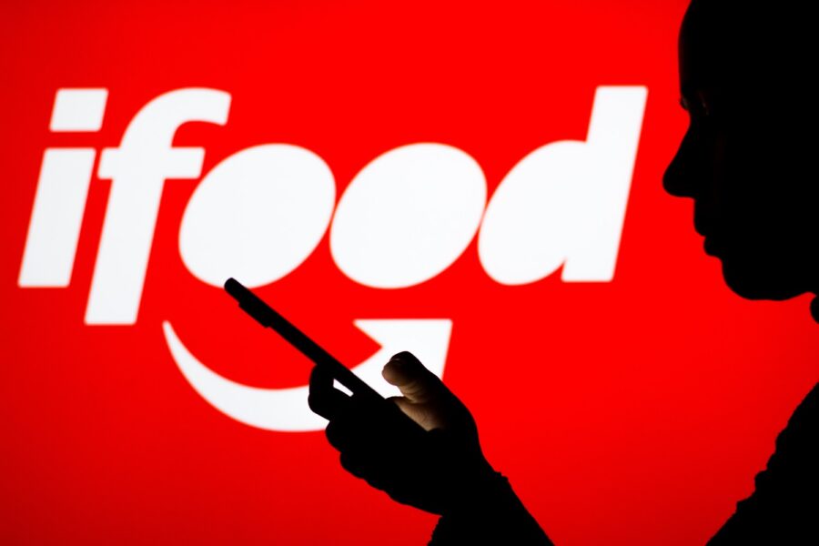 Pessoa mexendo no celular com logotipo do iFood ao fundo
