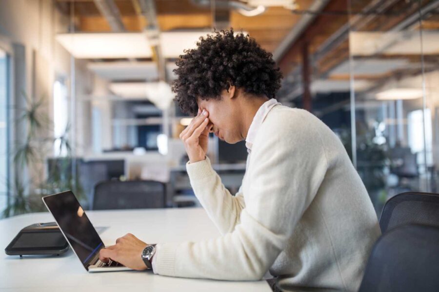 Pessoa mexendo no computador e com a mão nos olhos