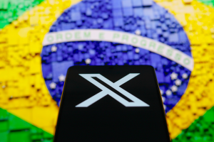 Celular com logo do X (Twitter) em frente a uma ilustração da bandeira do Brasil