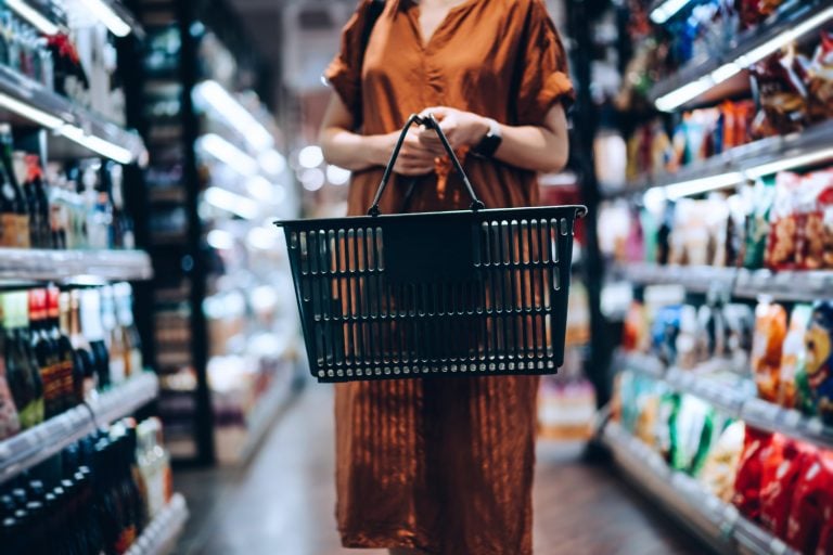 Mulher carrega uma cesta em um corredor de supermercado