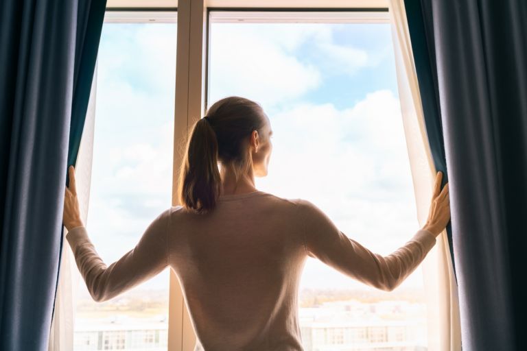 Mulher abrindo uma janela e olhando o horizonte