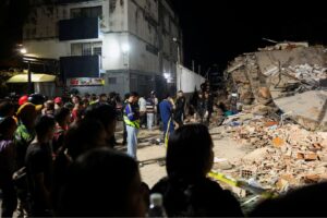 Pessoas se reúnem enquanto equipes de emergência atuam no local de prédio desabado em Caracas após terremotos 25 de junho de 2026