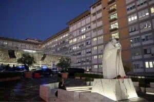 Um homem está sentado perto da estátua do falecido Papa João Paulo 2º, em frente ao Hospital Gemelli, onde o papa Leão está internado